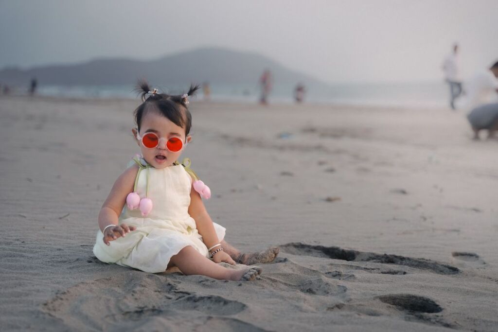 Bébé assis sur le sable, portant de petites lunettes de soleil rondes à monture plate