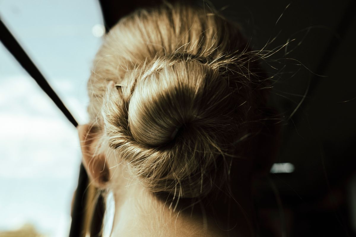 Un chignon serré ou une tresse ouvre une ligne de peau nue sur le sommet du crâne.