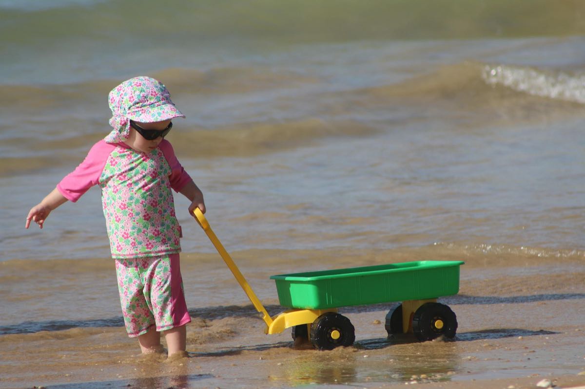Jeune enfant en haut à manches longues, chapeau à bavolet et lunettes de soleil au bord de l'eau