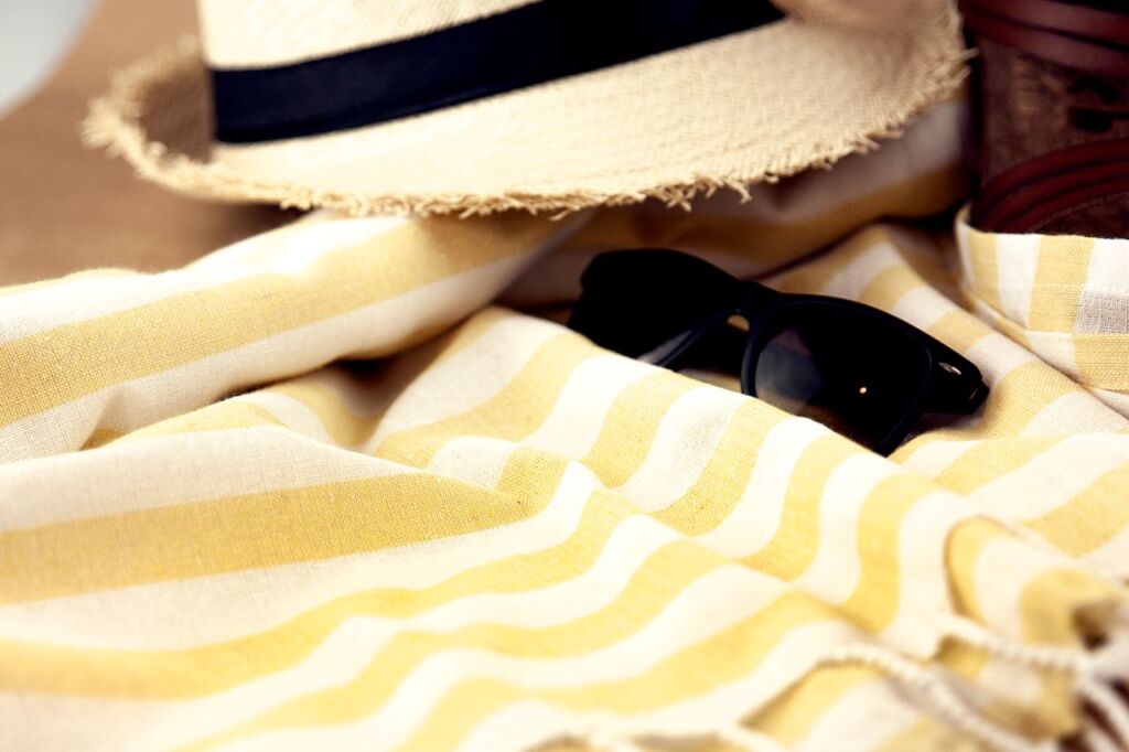 Chapeau de paille et lunettes de soleil posés sur une serviette de plage rayée
